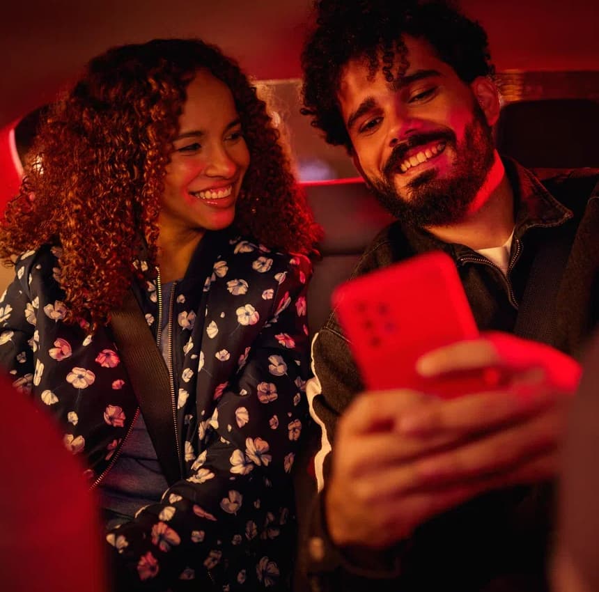 A happy man and a happy woman inside a car looking at a phone